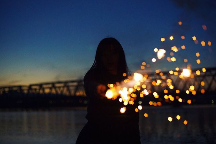 Close-up of illuminated woman against river at sunset