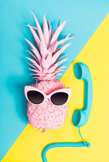 Close-up of sunglasses on pineapple with telephone receiver on colored background