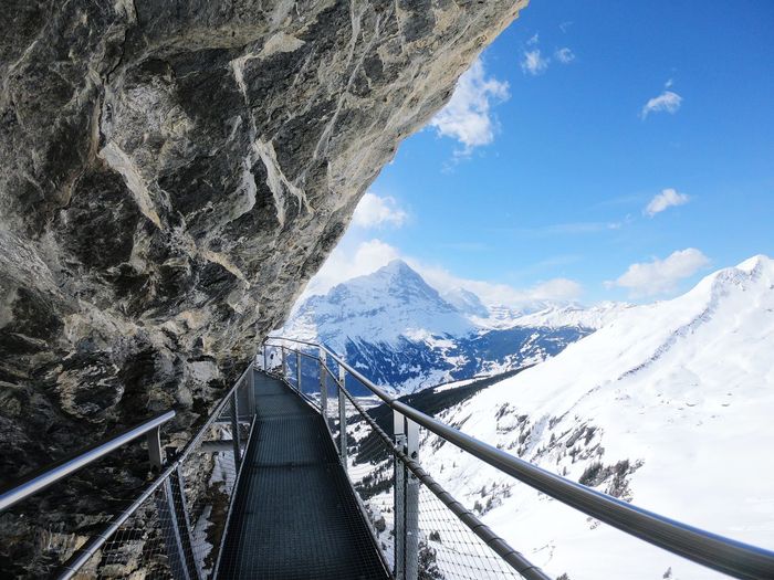Footbridge at snowcapped mountains against sky