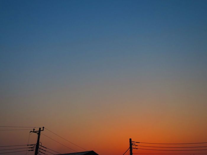 Low angle view of silhouette electricity poles during sunset