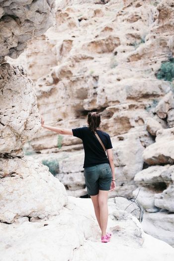 Full length rear view of young woman standing by rock formation