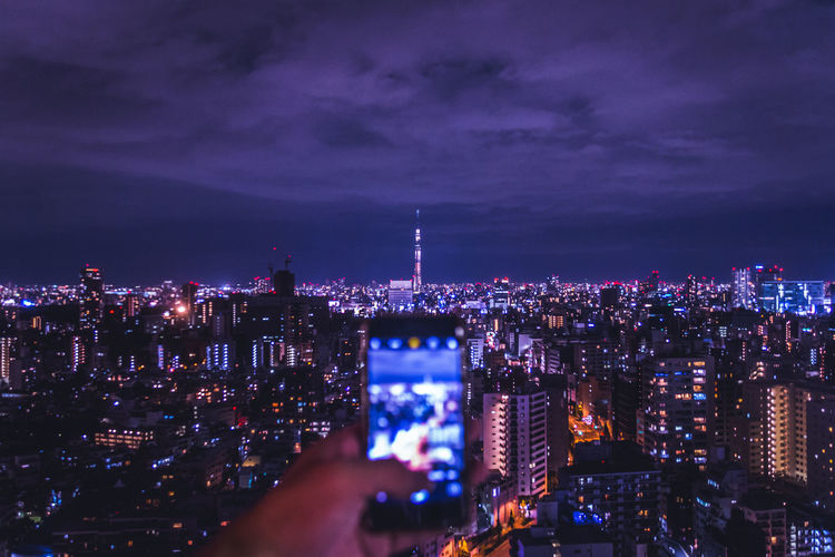 Cropped image of hand photographing illuminated cityscape at night