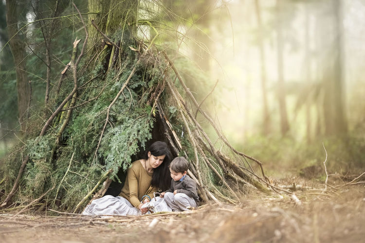 Mother with son sitting by plants tent in forest