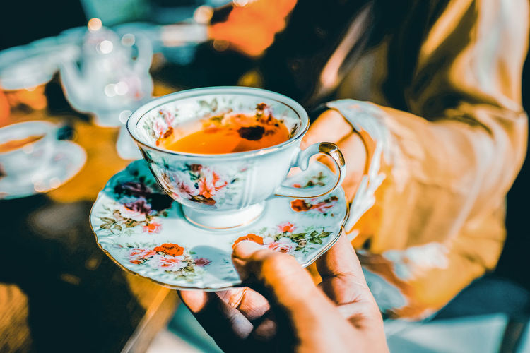 Cropped hand giving tea cup to woman