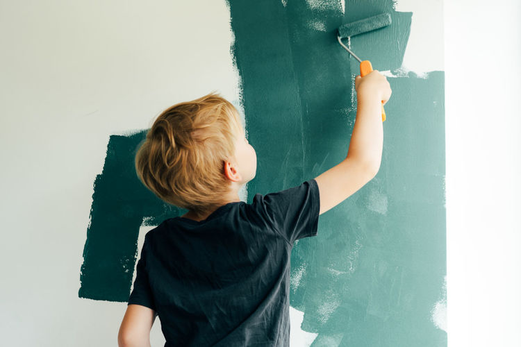 Rear view of boy painting on wall at home