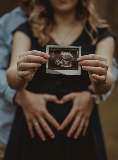 Midsection of pregnant woman holding ultrasound photo while standing with husband