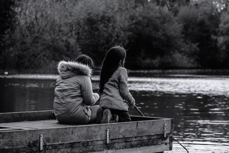 Rear view of woman with daughter sitting on pier over lake