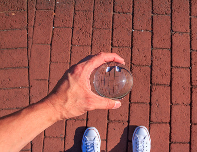 Low section of man holding crystal ball while standing on footpath