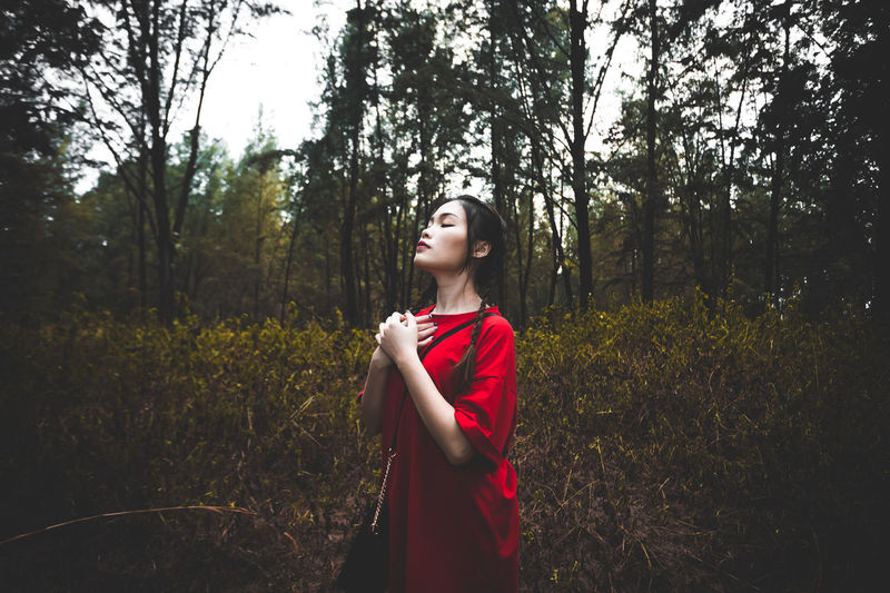 Young woman looking away while standing on land in forest