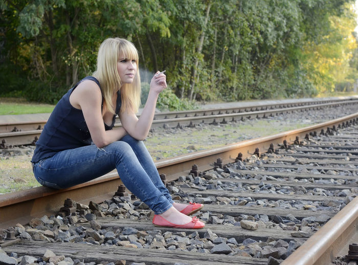 Full length of woman smoking while sitting on railroad track