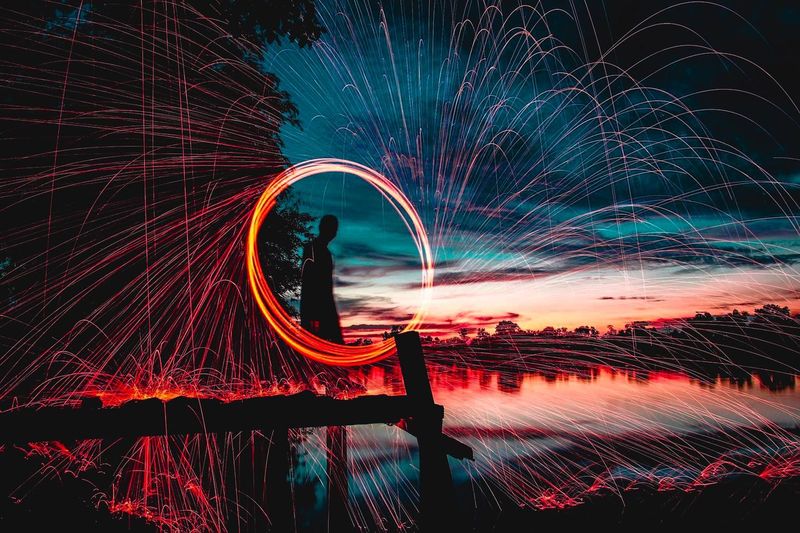 Silhouette man spinning lit wire wool on pier in lake