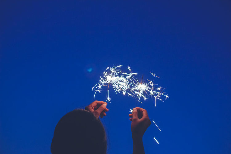 Rear view of woman holding sparklers against clear sky at night