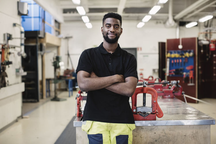 Portrait of smiling auto mechanic student standing arms crossed in workshop