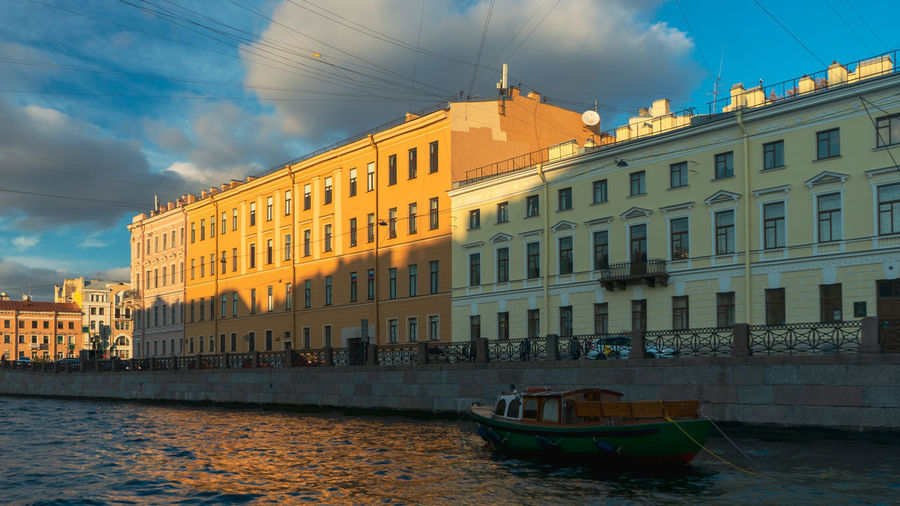Boats in river by buildings in city against sky