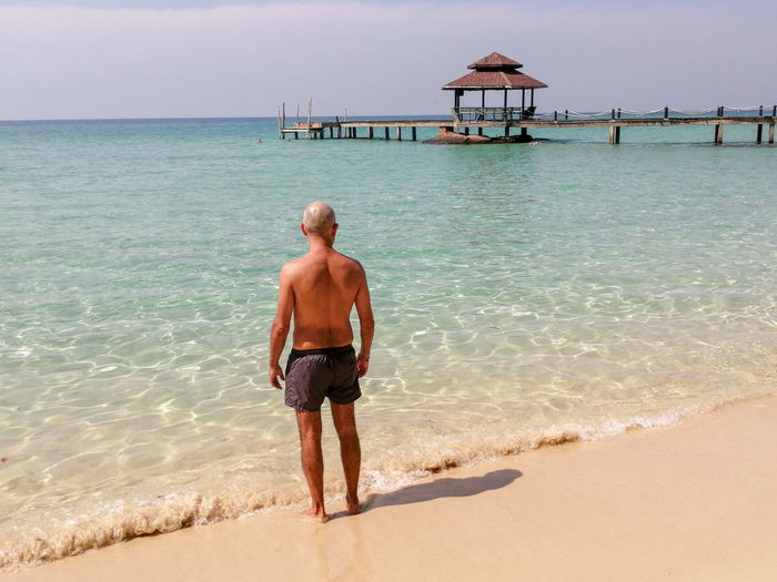 Rear view of shirtless man standing on beach, ko kut island, thailand 