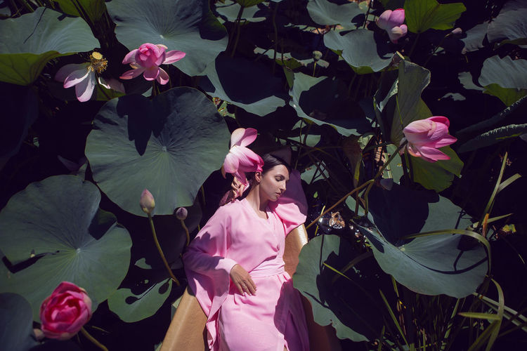 Portrait brunette woman  in a pink dress lie on a boat in the river among the lotuses in summer