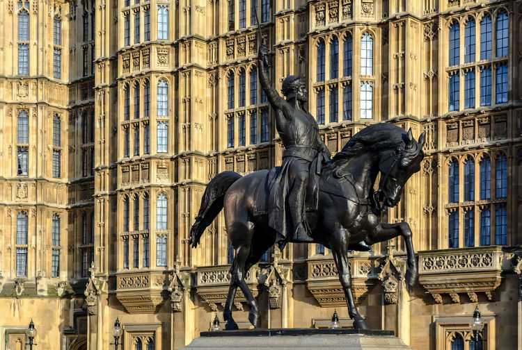 Equestrian statue of richard coeur de lion against palace of westminster walls in london.