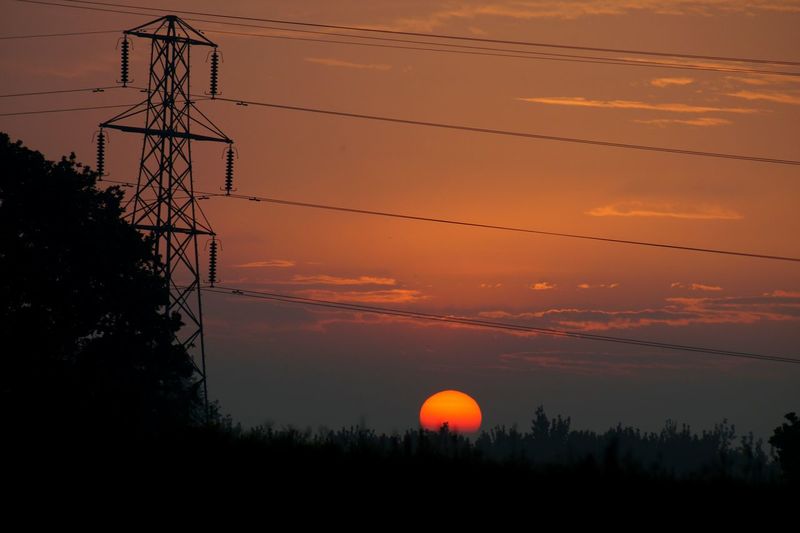 Silhouette trees and electricity pylon against romantic sky at sunset