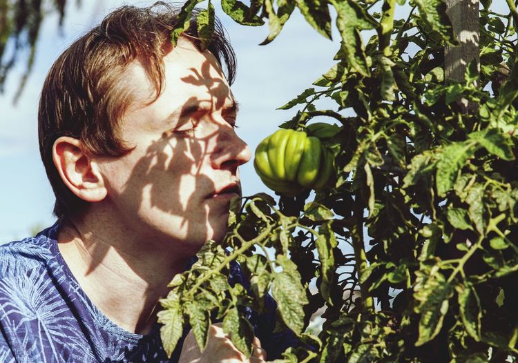 Portrait of man smelling tomato against sky