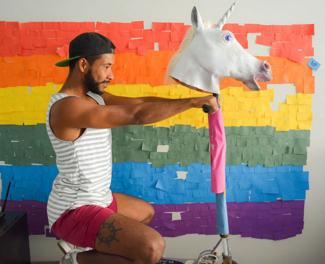 Man riding push scooter with unicorn against colorful wall