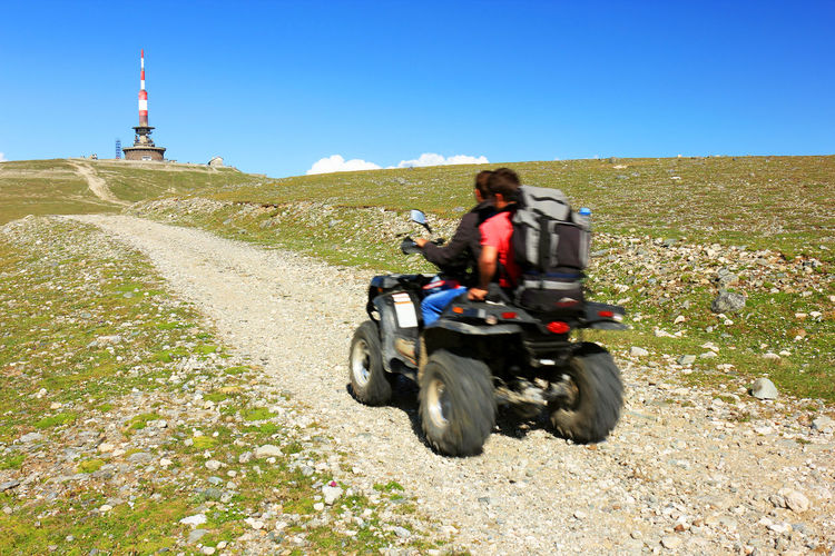 Friends riding quadbike on dirt road leading towards lighthouse at bucegi mountains