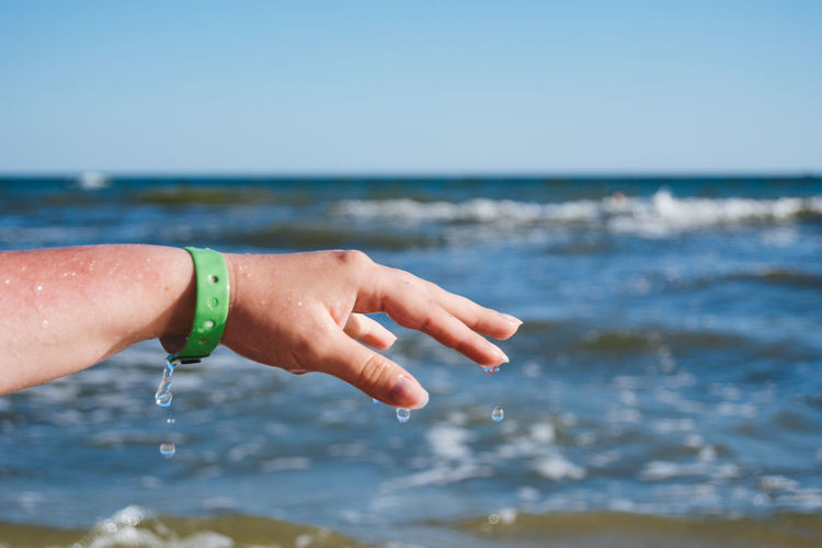 Cropped image of wet hand against sea