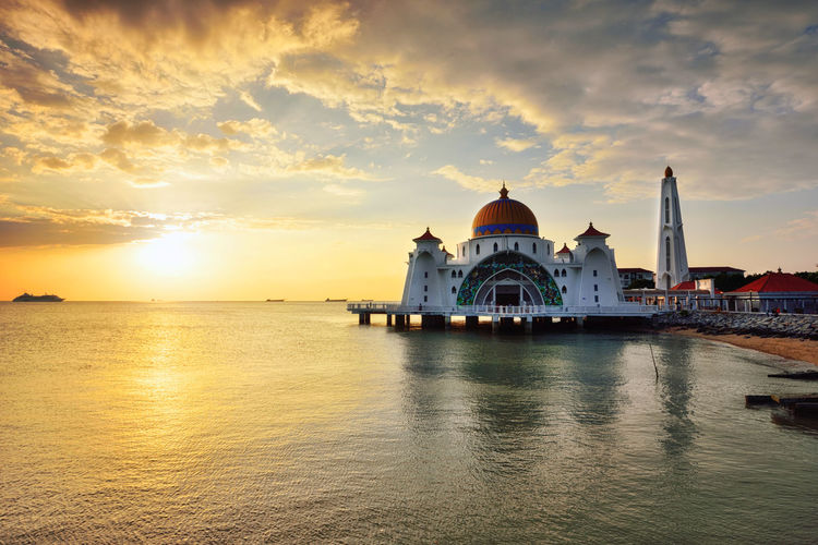 Scenic view of mosque by sea against sky during sunset