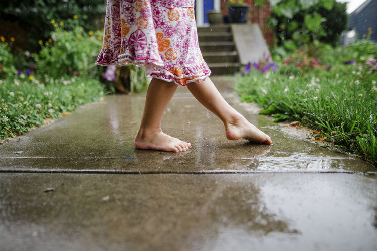Close-up of a small barefoot child dancing on front stoop in the rain