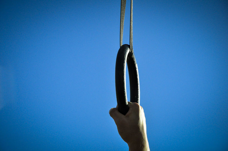Close-up of hand holding rope against blue sky