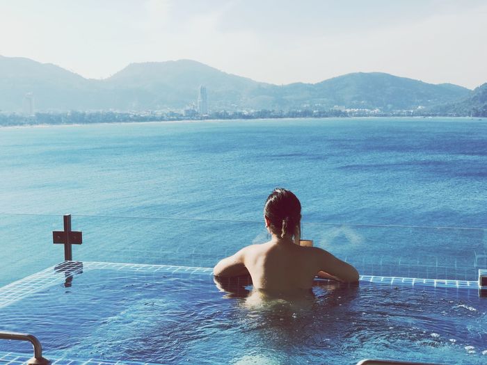 Rear view of shirtless woman in infinity pool against sky