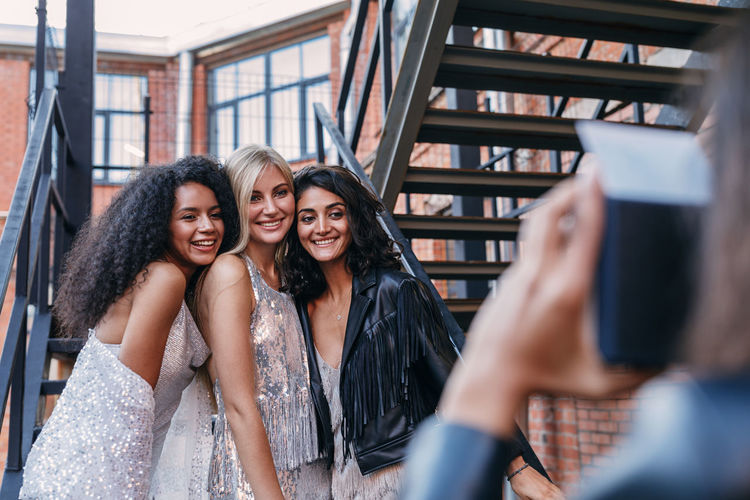 Cropped image of woman photographing happy female friends standing on staircase