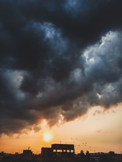 Silhouette buildings against dramatic sky during sunset