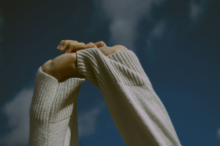 Close-up of woman stretching hands against sky