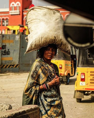 Poor woman carrying sack on head in city