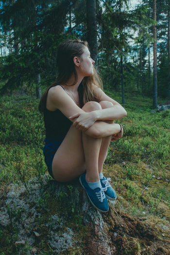 Young woman sitting on rock in forest