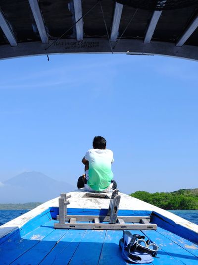 Rear view of man sitting on boat against blue sky