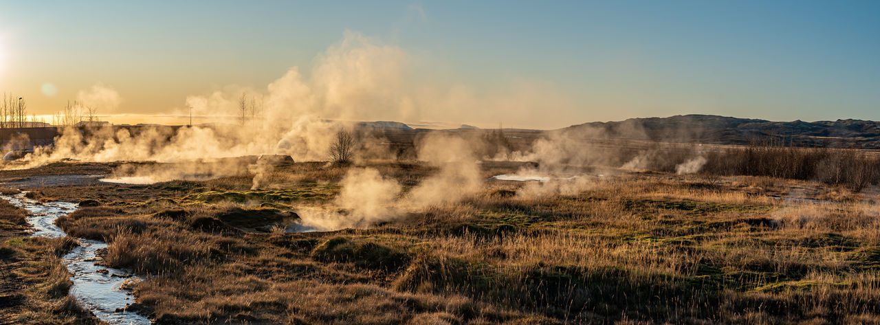 Panoramic view of steaming pot holes landscape against blue sky