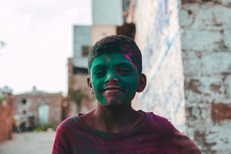 Portrait of smiling boy with green powder paint on face in town during holi