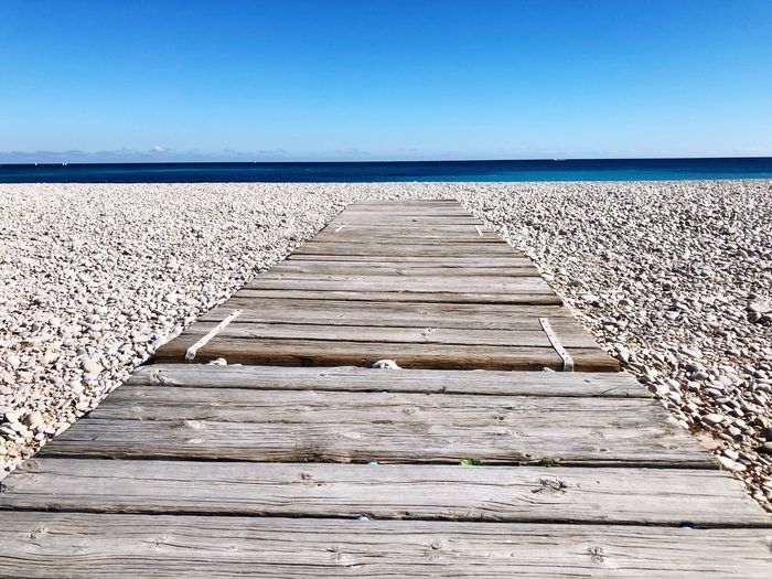 Boardwalk leading towards sea against clear blue sky