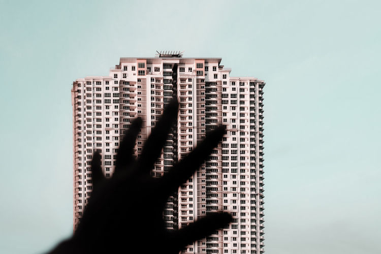 Cropped hand gesturing towards modern building against clear sky