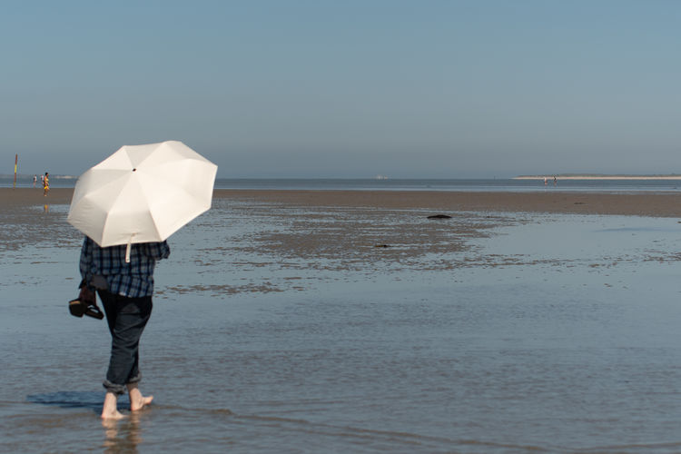 Full length of woman with umbrella standing on low tide beach 
