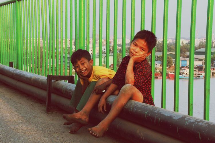 Portrait of boys sitting on pipe by railing