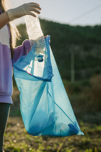 Woman putting plastic bottle in blue garbage bag