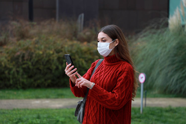Young woman wearing mask using mobile phone outdoors