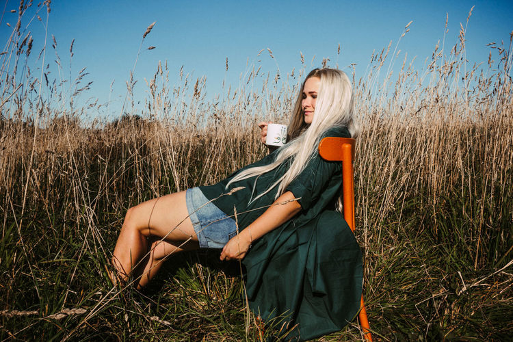 Young woman with mug sitting on chair amidst grass