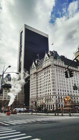 Smoke emitting by plaza hotel against cloudy sky in city