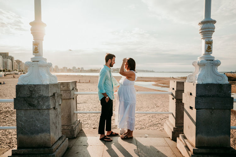 Full length of couple embracing while standing on beach against sky