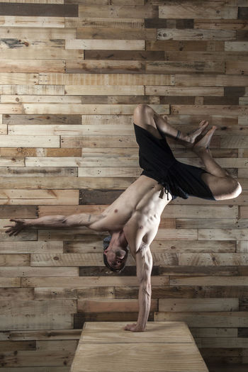 Full length of shirtless man against wooden wall