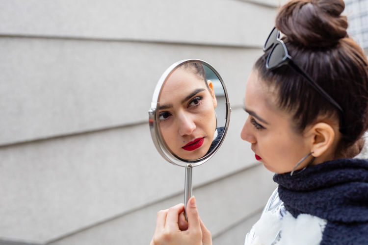 Close-up of young woman looking at mirror with reflection against wall