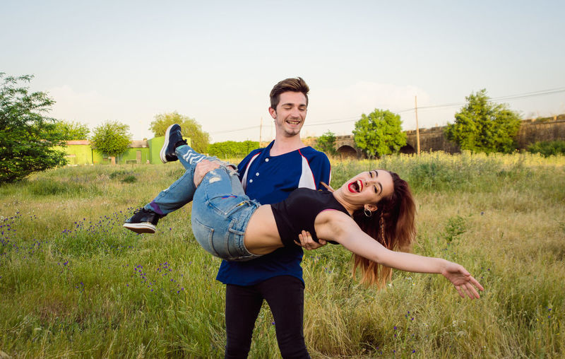 Boyfriend carrying girlfriend while standing on grassy field